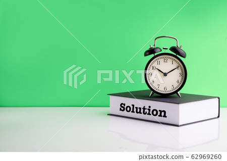 SOLUTION text, Alarm Clock and book on green 62969260