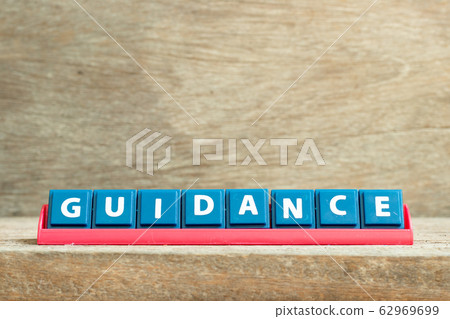 Tile letter on red rack in word guidance on wood background Tile letter on red rack in word guidance on wood background 62969699