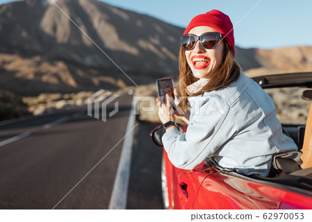 Woman leaning out of the car with smartphone on the roadside 62970053