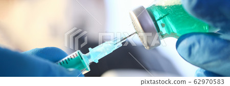 Scientist hand in blue protective gloves filling syringe with some experimental liquid Scientist hand in blue protective gloves filling syringe with some experimental liquid 62970583