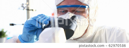 Man wearing sterile protective suit analysing something using microscope Man wearing sterile protective suit analysing something using microscope 62970586