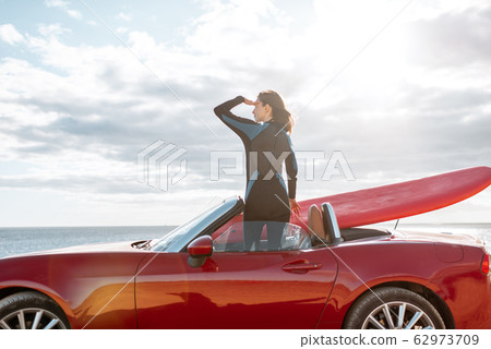 Woman with surfboard on the car near the ocean 62973709