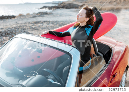 Woman with surfboard on the car near the ocean 62973713