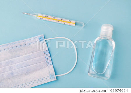 Disposable surgical mask, thermometer and antibacterial hand gel on a blue background. 62974634