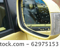 Drops of rain soaked in the rearview mirror of a yellow car 62975153