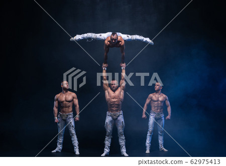 Four muscular man perform difficult acrobatic tricks on black studio  62975413