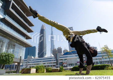 Acrobat keep balance one the hands with blurred Dubai cityscape. Concept of modern, business and Acrobat keep balance one the hands with blurred Dubai cityscape. Concept of modern, business and 62975455