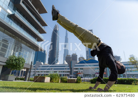 Acrobat keep balance one the hands with blurred Dubai cityscape. Concept of modern, business and 62975480