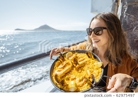Woman eating sea food near the ocean Woman eating sea food near the ocean 62975497