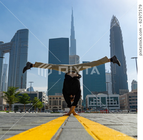 Acrobat keep balance one the hands with blurred Dubai cityscape. Concept of modern, business and Acrobat keep balance one the hands with blurred Dubai cityscape. Concept of modern, business and 62975579