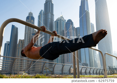 Muscular man doing workout on the street with cityscape of skyscrapers on background in Dubai Muscular man doing workout on the street with cityscape of skyscrapers on background in Dubai 62975759