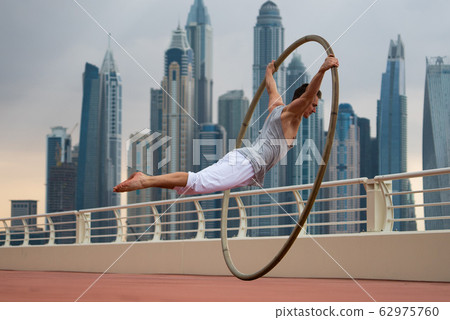 Cyr Wheel artist with cityscape background of Dubai during sunset Cyr Wheel artist with cityscape background of Dubai during sunset 62975760