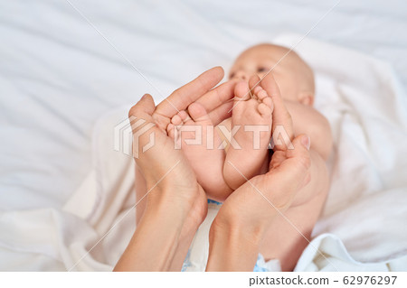 Young adult woman holding little new born baby feet in hands Young adult woman holding little new born baby feet in hands 62976297