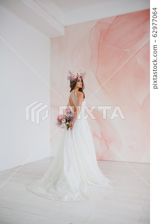 Young bride in white dress with flower wreath on her head posing in the studio 62977064