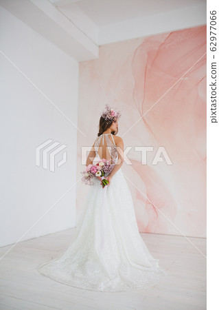 Young bride in white dress with flower wreath on her head posing in the studio Young bride in white dress with flower wreath on her head posing in the studio 62977066