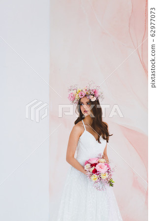 Young bride in white dress with flower wreath on her head posing in the studio Young bride in white dress with flower wreath on her head posing in the studio 62977073