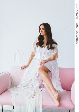 Young bride in white negligee posing on the rose sofa in the studio 62977086