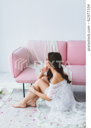 Young bride in white negligee posing near the rose sofa in the studio Young bride in white negligee posing near the rose sofa in the studio 62977104