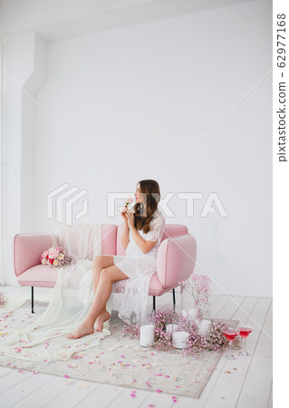 Young bride in white negligee posing on the rose sofa in the studio Young bride in white negligee posing on the rose sofa in the studio 62977168
