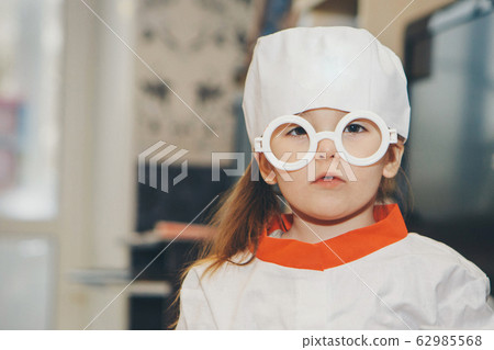 a little girl in a doctor's suit. The child is playing doctor. White coat, glasses, cap with a red cross, medical equipment. Concept of a healthy lifestyle, health care, medicine 62985568