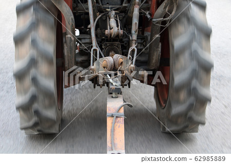 An old tractor ride on asphalt road and pulls a An old tractor ride on asphalt road and pulls a 62985889
