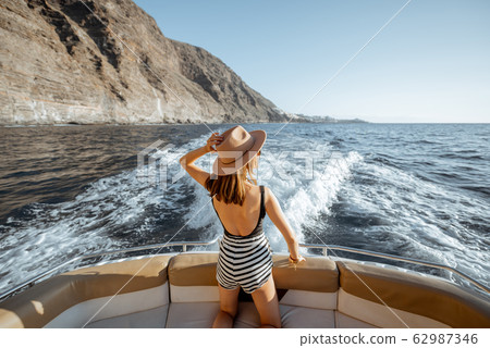 Relaxed woman sailing on the yacht near the rocky coast 62987346