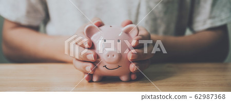 Panoramic image, Man hand holding piggy bank on wood table Panoramic image, Man hand holding piggy bank on wood table 62987368