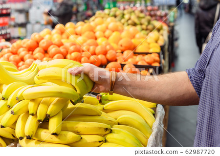 mans hand take bananas from shelf of store. healthy food. shopping concept mans hand take bananas from shelf of store. healthy food. shopping concept 62987720