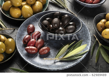 Olives, green, black and red, an assortment with leaves on a black background Olives, green, black and red, an assortment with leaves on a black background 62989489