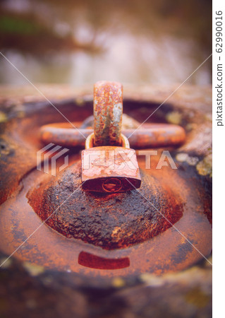Rusty padlock locked around an aged iron ring Rusty padlock locked around an aged iron ring 62990016