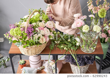 Floral shop concept . Florist woman creates flower arrangement in a wicker basket. Beautiful bouquet of mixed flowers. Handsome fresh bunch. Flowers delivery. Floral shop concept . Florist woman creates flower arrangement in a wicker basket. Beautiful bouquet of mixed flowers. Handsome fresh bunch. Flowers delivery. 62990243