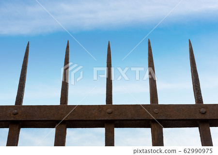 Wrought iron fence with sharp points on blue sky with clouds 62990975