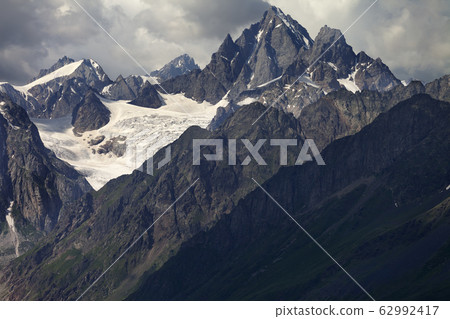 High rocky mountains with glacier in storm clouds High rocky mountains with glacier in storm clouds 62992417