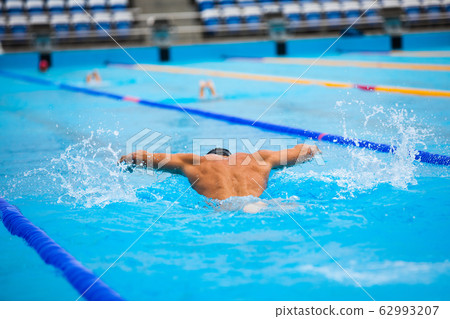 Athletic man swimming in butterfly style in the swimming pool with clear blue water. 62993207