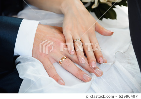 hands of bride and groom with wedding gold rings on white dress 62996497