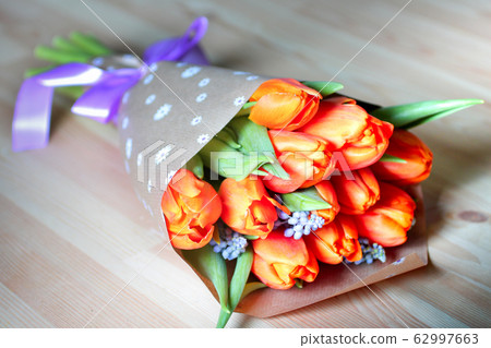 beautiful orange tulips bouquet in wrapping paper with ribbon on wooden table 62997663