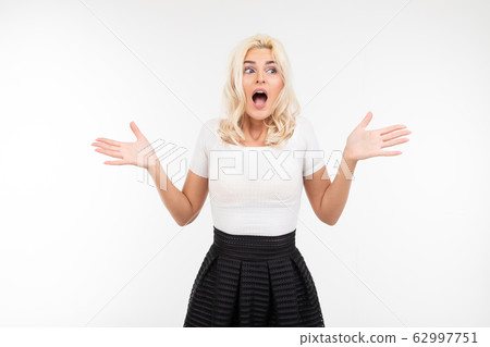 portrait of a surprised blond girl in a white T-shirt waving her arms to the sides on a white portrait of a surprised blond girl in a white T-shirt waving her arms to the sides on a white 62997751