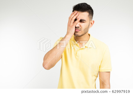 Caucasian man in a yellow T-shirt is having a headache on a white studio background Caucasian man in a yellow T-shirt is having a headache on a white studio background 62997919