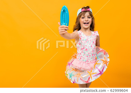Beautiful little girl in swinsuit holds a rubber ring and shows a thermometer for a water isolated 62999604