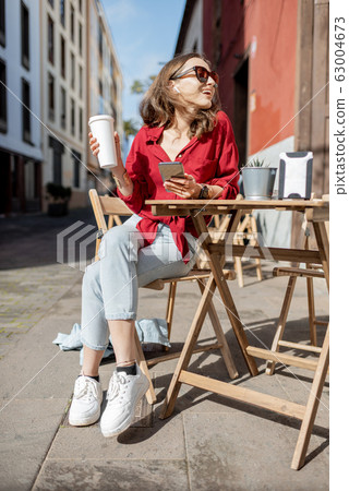 Woman with phone and coffee on the cafe terrace outdoors 63004673