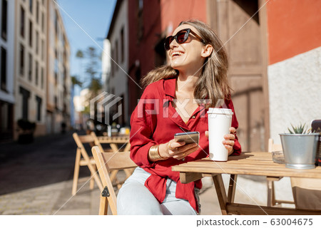 Woman with phone and coffee on the cafe terrace outdoors 63004675