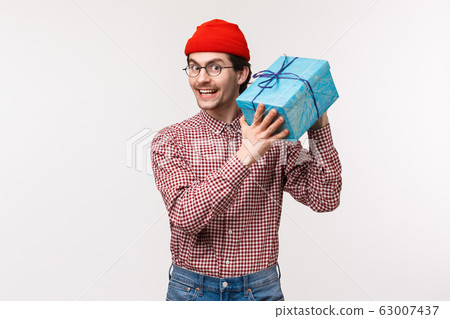 Waist-up portrait happy and excited cute bearded guy trying guess whats inside box, shaking wrapped gift curious what friend give him for b-day, smiling delighted and cheerful, stand white background Waist-up portrait happy and excited cute bearded guy trying guess whats inside box, shaking wrapped gift curious what friend give him for b-day, smiling delighted and cheerful, stand white background 63007437