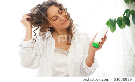 Pretty woman showing white cosmetic tube for curly hair care in hand Pretty woman showing white cosmetic tube for curly hair care in hand 63008959