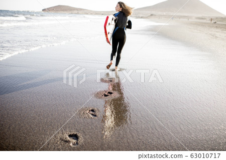 Young surfer with surfboard on the beach 63010717