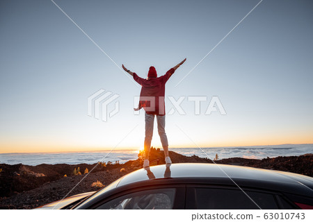 Woman traveling by car on the rocky terrain above the clouds on a sunset 63010743