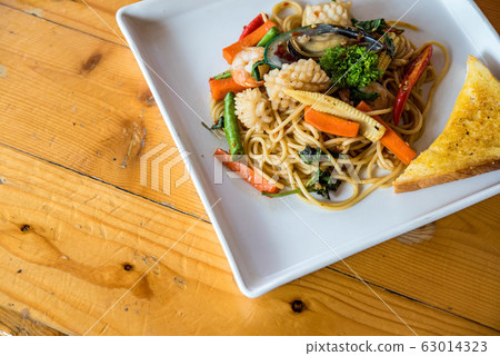 Seafood spaghetti, shrimp, squid, vegetables Asian cuisine is popular on white plates on wooden floors. Seafood spaghetti, shrimp, squid, vegetables Asian cuisine is popular on white plates on wooden floors. 63014323