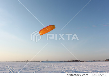 Orange kite in the sky above the snowy surface Orange kite in the sky above the snowy surface 63017252