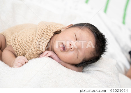 Happy cute adorable Asian baby boy with black hair lying a white blanket. 63021024