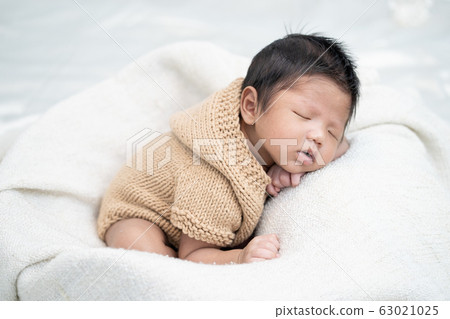 Happy cute adorable Asian baby boy with black hair lying on a white blanket. 63021025