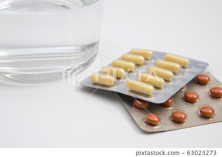 Pills and glass of water on white background. 63023273